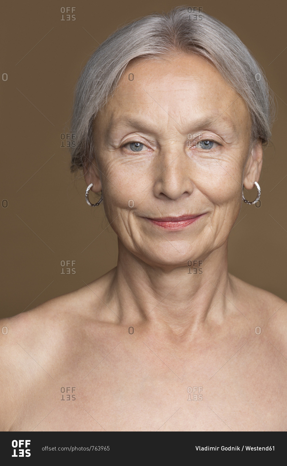 Portrait Of Naked Senior Woman With Grey Hair In Front Of Brown Portrait Of Naked Senior Woman With Grey Hair In Front Of Brown